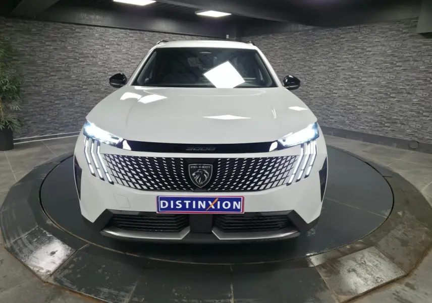 Peugeot 5008 blanc vue de face en intérieur, avec calandre noire à motif et feux LED allumés.