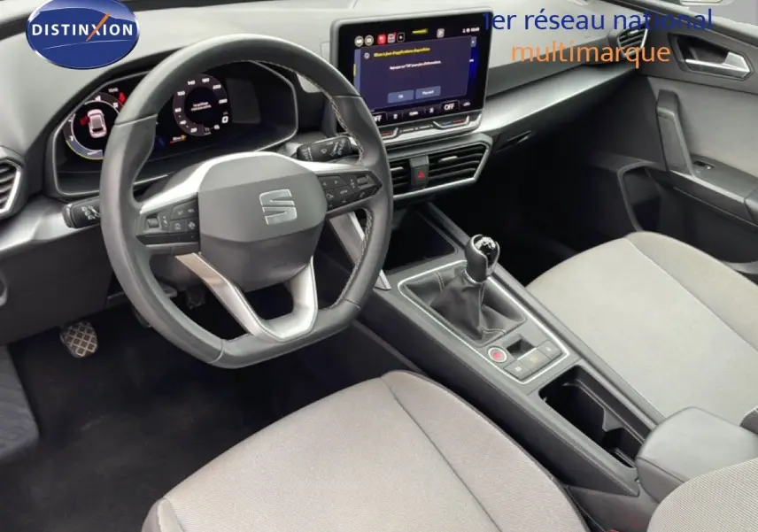 Vue intérieure centrée sur le poste de conduite du SEAT LEON 2025, volant cuir, tableau de bord digital et levier manuel.