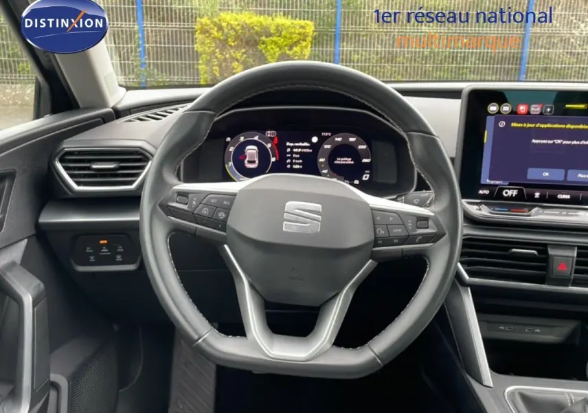 Vue intérieure centrée sur le volant cuir et le tableau de bord numérique d'une SEAT LEON gris métallique.