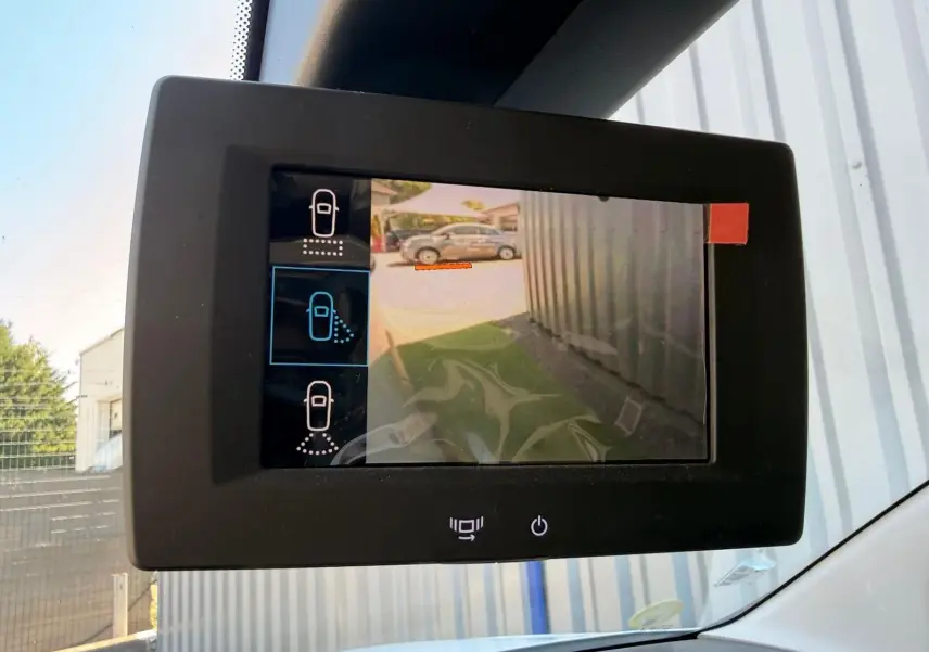 Écran intérieur affichant la caméra de recul du Citroën Berlingo blanc, vue latérale droite en stationnement.