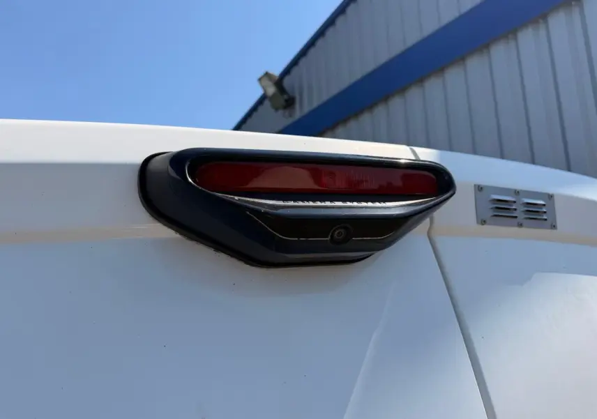 Gros plan sur la caméra de recul intégrée au feu stop arrière noir du Citroën Berlingo Van blanc, vue de dos.