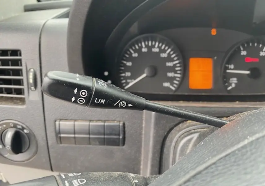 Gros plan sur la commande du régulateur et limiteur de vitesse dans le tableau de bord noir d'un Mercedes Sprinter blanc.