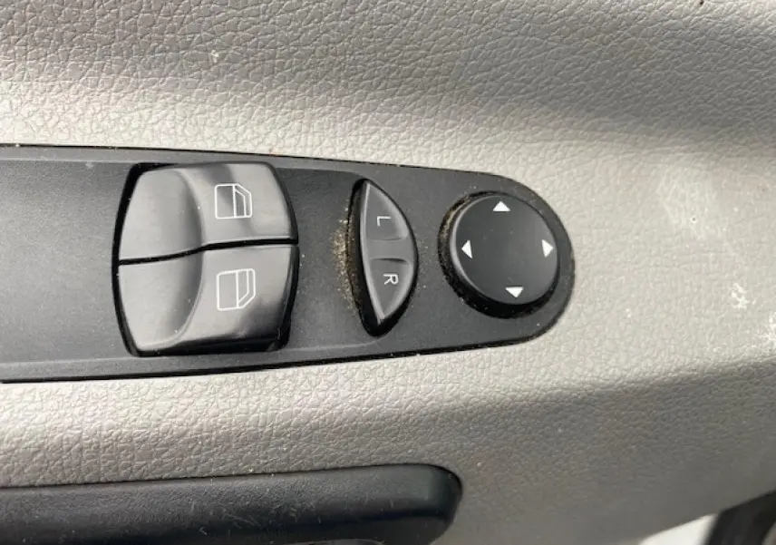 Boutons de commande des lève-vitres et réglages électriques des rétroviseurs sur la porte côté conducteur d’un Mercedes Sprinter blanc.