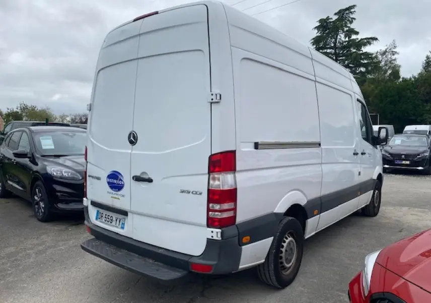 Vue 3/4 arrière droite d'un fourgon Mercedes Sprinter blanc de 2015 avec porte arrière fermée sur parking.