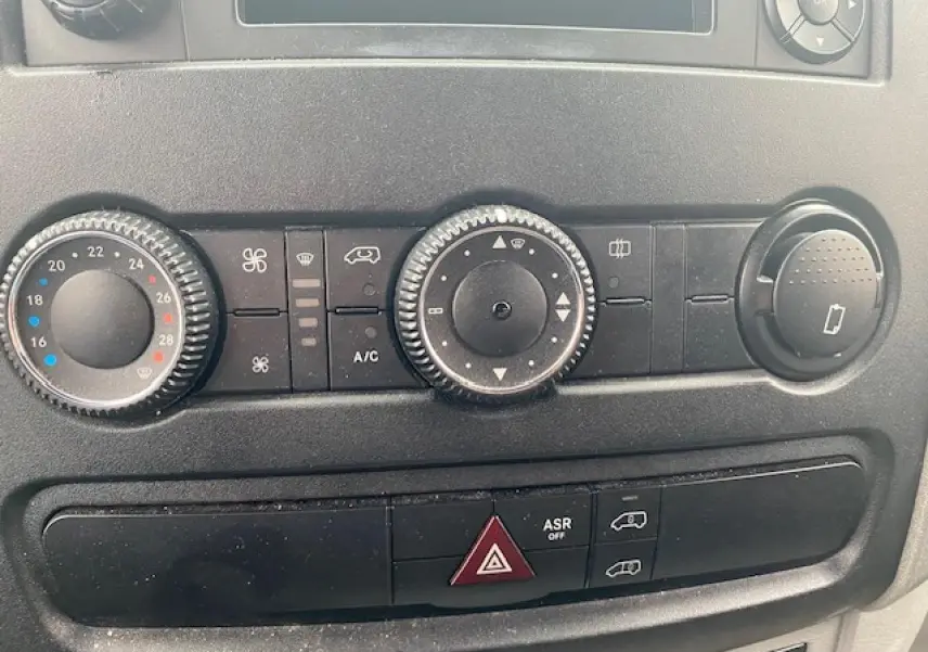 Gros plan sur les commandes de climatisation et les boutons de sécurité du tableau de bord du Mercedes Sprinter blanc.