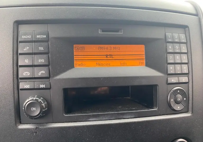 Gros plan sur la radio orange allumée du tableau de bord d'un Mercedes Sprinter Fourgon blanc de 2015.