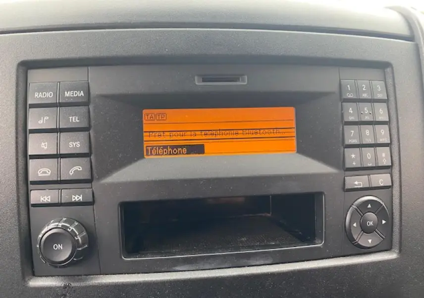 Console centrale du Mercedes Sprinter Fourgon 2015 avec écran orange affichant la fonction téléphone Bluetooth.