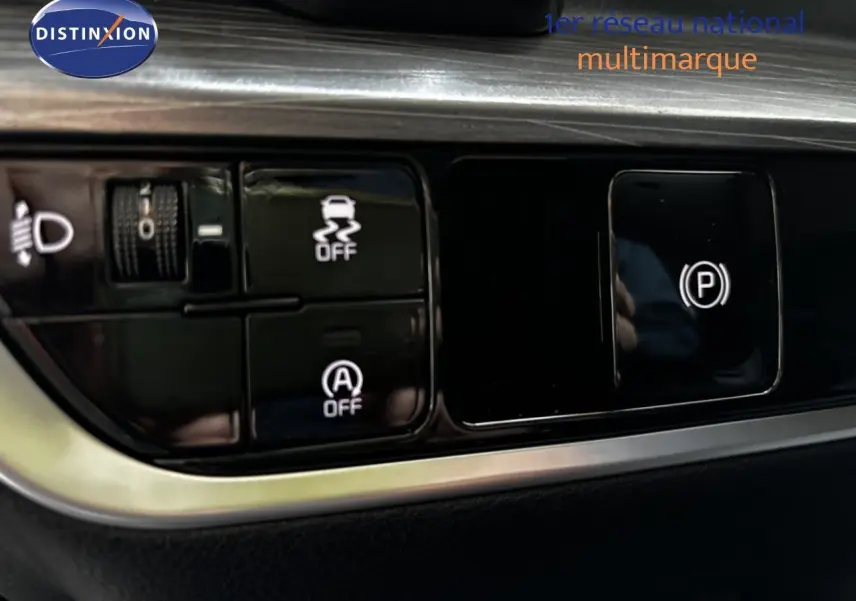 Gros plan sur les commandes noires du tableau de bord du Kia Sportage blanc nacré, avec boutons de stabilité et frein à main électronique.