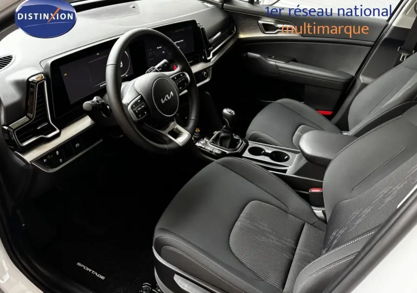 Vue intérieure avant du Kia Sportage 2025 blanc nacré, sièges noirs et tableau de bord moderne avec boîte manuelle.