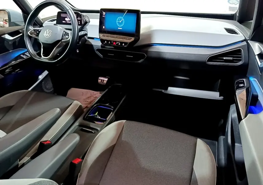 Vue intérieure avant du Volkswagen ID.3 77 kWh Pro S, tableau de bord clair avec écran tactile central et éclairage d'ambiance bleu.