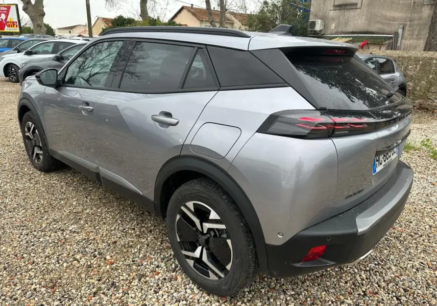 Vue 3/4 arrière droite d'un Peugeot 2008 Hybrid gris avec barres de toit et jantes alliage 17 pouces.