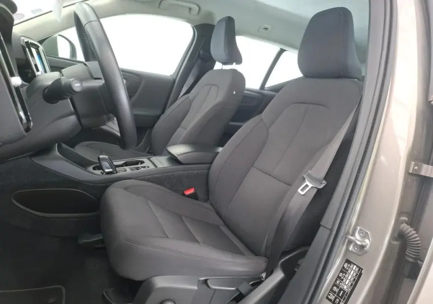 Vue intérieure côté conducteur du Volvo XC40 marron clair 2021, montrant les sièges avant en tissu gris et le tableau de bord.