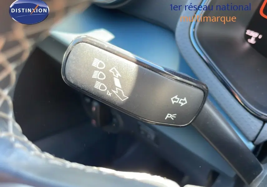 Gros plan sur la commande des clignotants et feux du SEAT Arona 2025, intérieur noir avec volant partiellement visible.