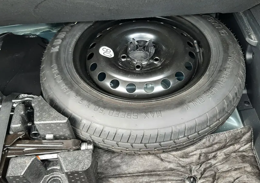 Vue rapprochée de la roue de secours noire et du cric dans le coffre du Renault Arkana E-Tech Bleu Zanzibar 2021.