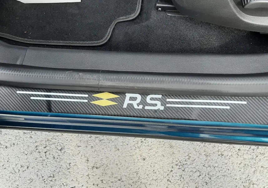 Vue rapprochée de la porte côté gauche du Renault Arkana Bleu Zanzibar, avec logo RS sur la plaque de seuil en carbone.