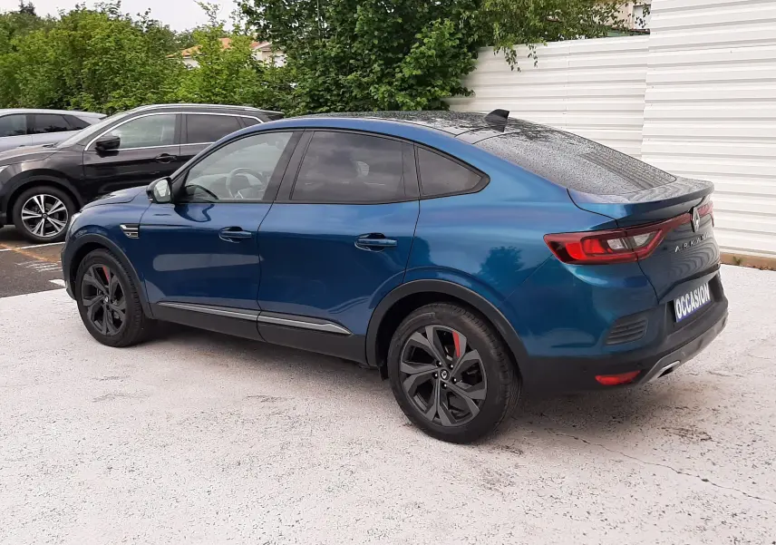 Vue 3/4 arrière droite d'un Renault Arkana E-Tech bleu Zanzibar avec jantes noires et feux LED, stationné en extérieur.