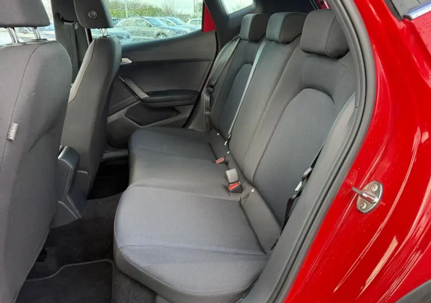 Vue intérieure côté arrière droit du SEAT Arona rouge 2024, montrant la banquette arrière en tissu gris foncé.
