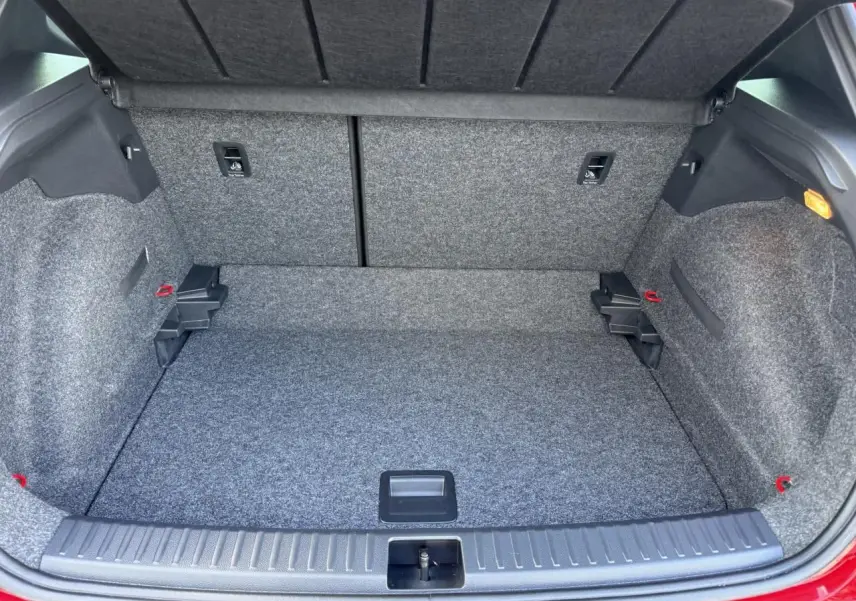 Coffre ouvert vu de l'arrière d'une SEAT Arona rouge 2024, montrant un espace de chargement propre et tapissé gris.
