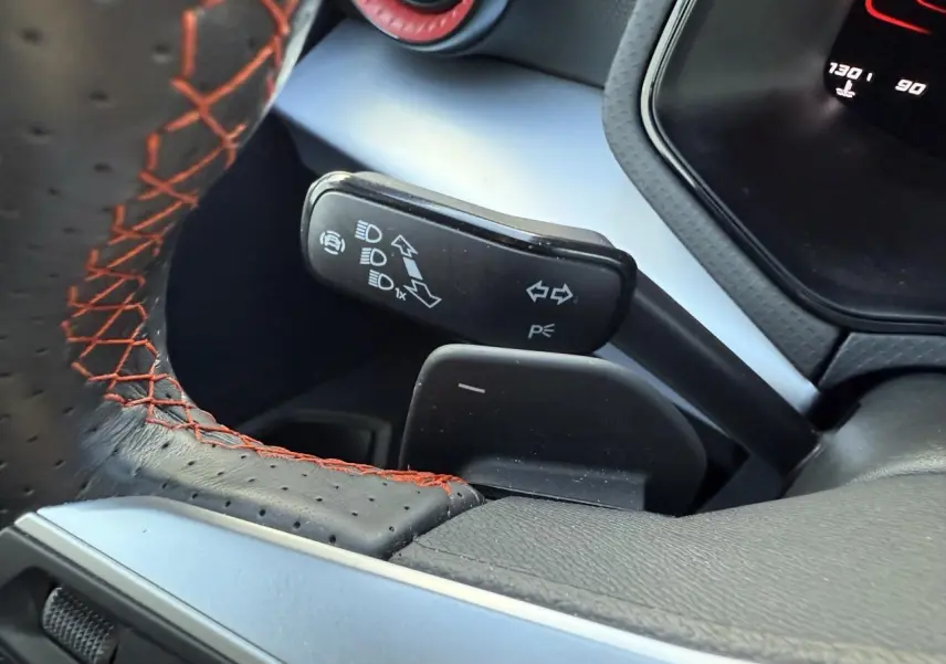 Gros plan sur le volant sport perforé noir avec surpiqûres rouges et la commande des clignotants du SEAT Arona 2024.