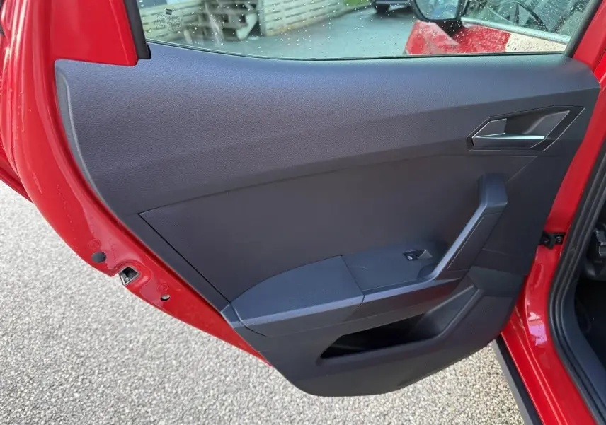 Vue rapprochée de la porte arrière gauche rouge du SEAT Arona 2024, montrant la garniture intérieure noire et la poignée.