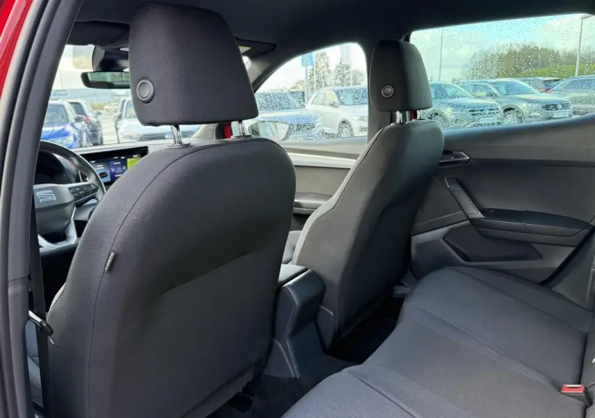Vue intérieure arrière du SEAT Arona rouge 2024, montrant les sièges noirs et la console centrale entre les sièges avant.