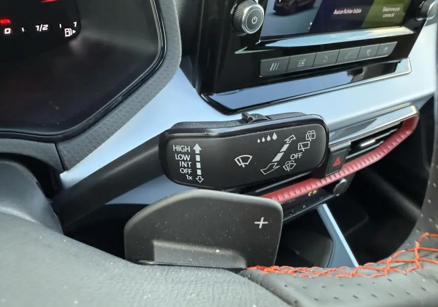 Gros plan sur la manette d’essuie-glace et palette de changement de vitesse côté gauche du tableau de bord noir avec surpiqûres rouges du SEAT Arona rouge.