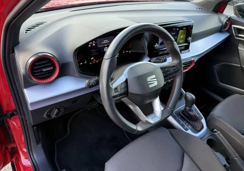 Vue intérieure côté conducteur du SEAT Arona rouge 2024, volant sport cuir Nappa avec surpiqûres rouges et tableau de bord digital.