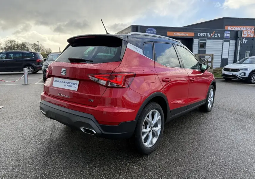 Vue 3/4 arrière droite d’un SEAT Arona rouge 2024 avec toit noir, jantes alliage et feux arrière LED triangulaires.