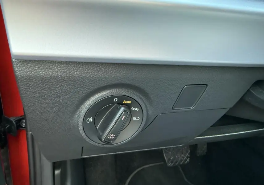 Détail du bouton de commande des phares sur le côté gauche du tableau de bord d’un SEAT Arona rouge 2024.
