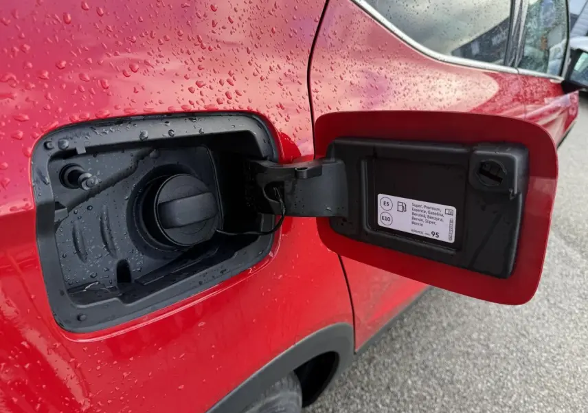 Vue rapprochée de la trappe à carburant rouge ouverte côté gauche d’un SEAT Arona 2024 avec gouttes d’eau.