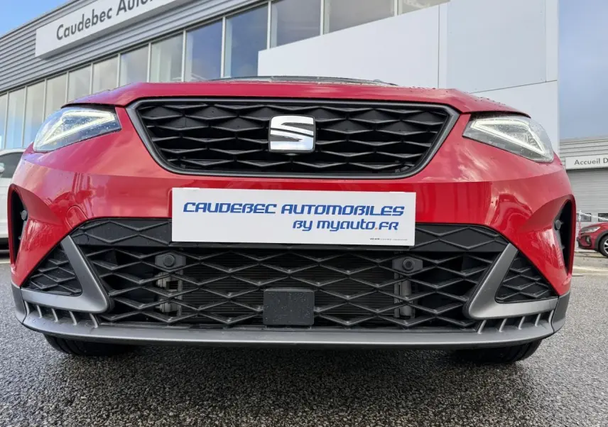 Vue avant rapprochée du SEAT Arona rouge 2024 avec calandre noire et phares Full LED allumés.