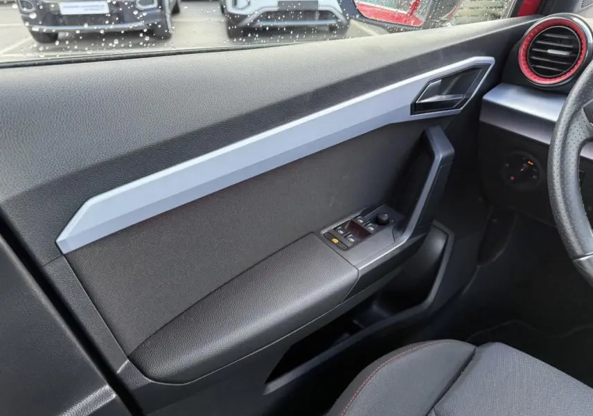Vue intérieure côté gauche de la porte avant d'un SEAT Arona 2024 avec commandes électriques et habillage noir et gris.