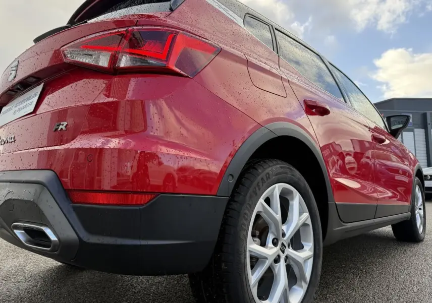 Vue 3/4 arrière droite d’un SEAT Arona rouge 2024 avec jantes alliage et feux arrière LED mouillés par la pluie.