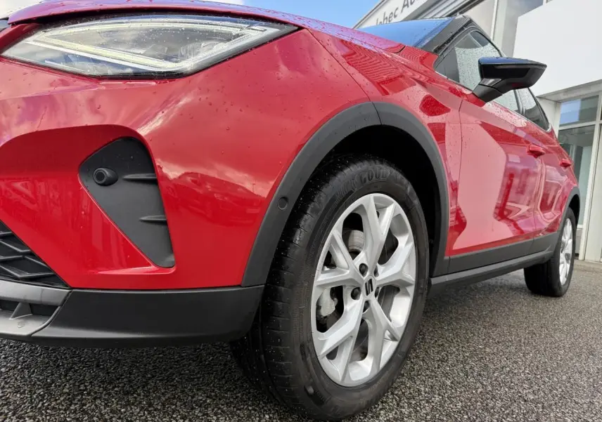 Vue en gros plan 3/4 avant droit d'un SEAT Arona rouge avec projecteur LED et jante alliage argentée.
