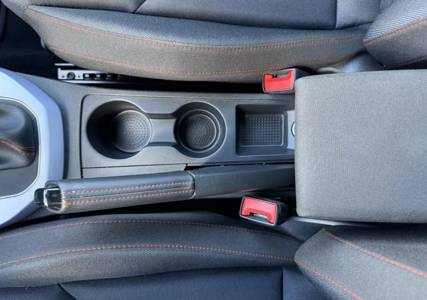 Vue plongeante sur la console centrale noire du SEAT Arona 2024 avec frein à main et porte-gobelets, surpiqûres rouges visibles.