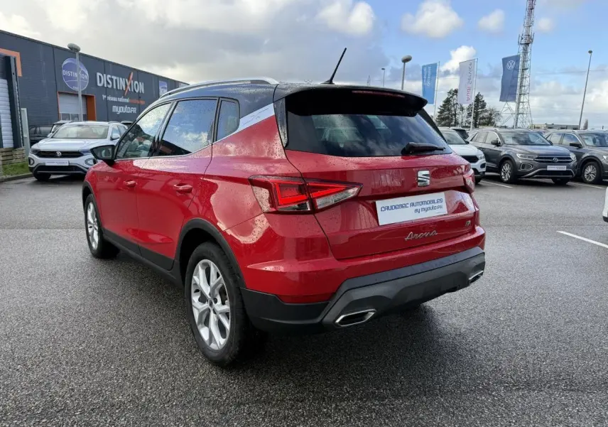 Vue 3/4 arrière droite d'un SEAT Arona rouge avec vitres surteintées et feux arrière LED, stationné sur parking humide.