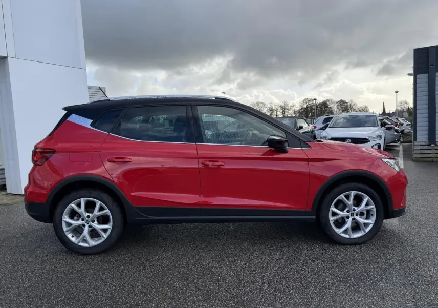 Profil droit d'un SEAT Arona rouge 2024 avec toit noir et jantes alliage argentées sur parking extérieur.