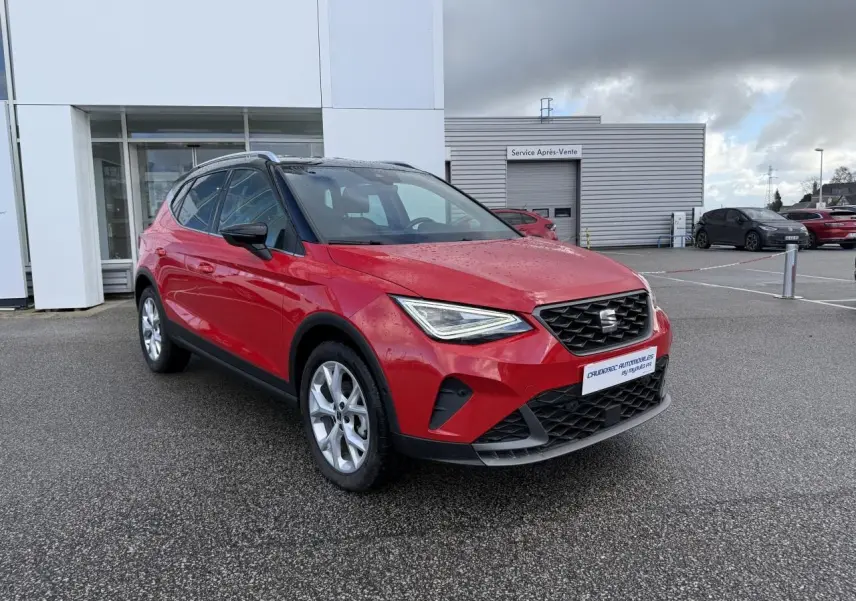 SEAT Arona rouge vue 3/4 avant droit, avec projecteurs LED et calandre noire, stationné devant un bâtiment.