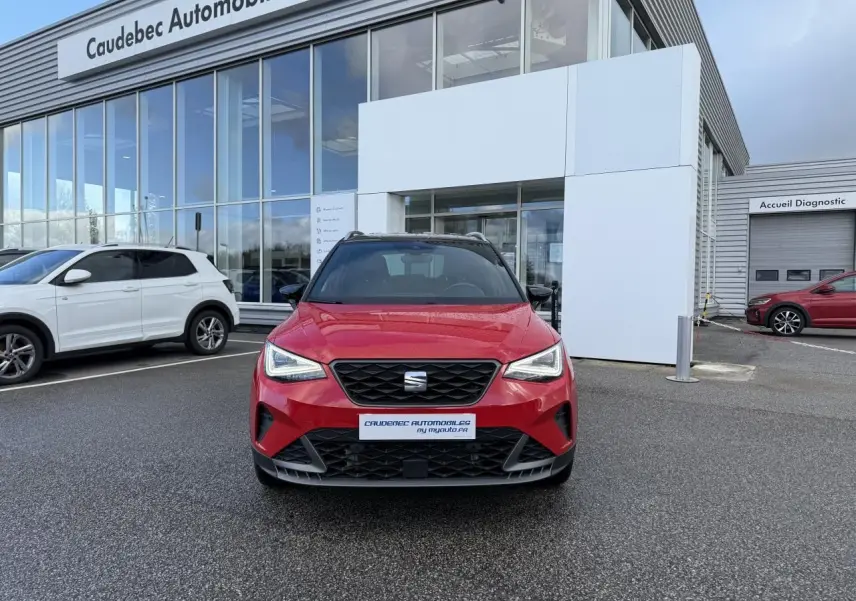 Vue frontale d’un SEAT Arona rouge avec calandre noire et projecteurs Full LED, stationné devant un concessionnaire.