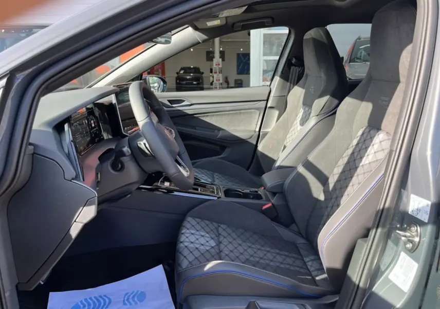 Vue intérieure côté conducteur de la Volkswagen Golf gris dauphin, sièges sport R-Line avec surpiqûres bleues et volant cuir multifonctions.