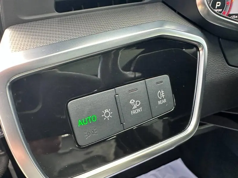Boutons de commande des phares avec indication "AUTO" verte sur tableau de bord noir brillant d'une Audi A6 Avant noir métal.