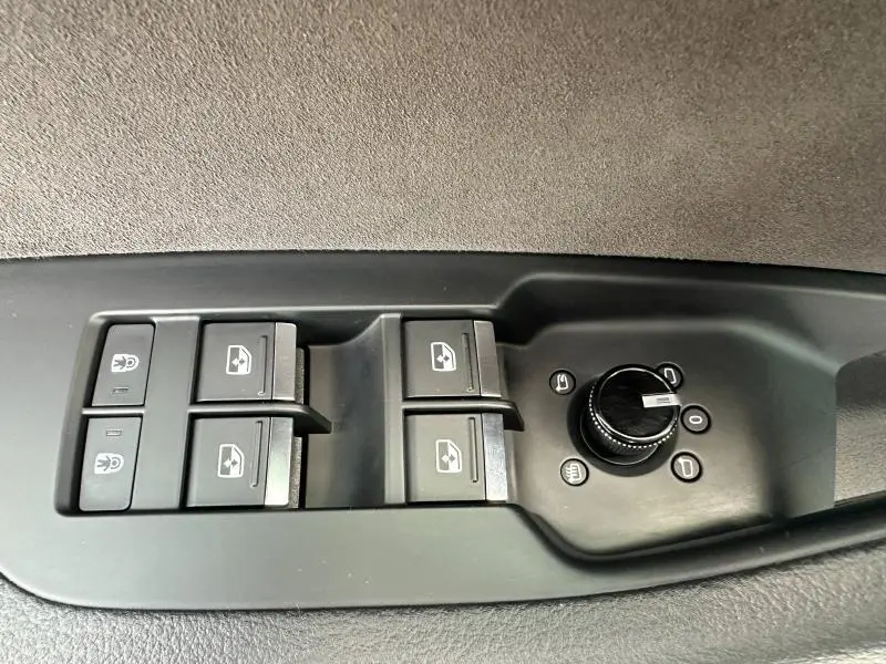 Gros plan sur les commandes de lève-vitres et réglage des rétroviseurs côté conducteur d'une Audi A6 Avant noir métal.