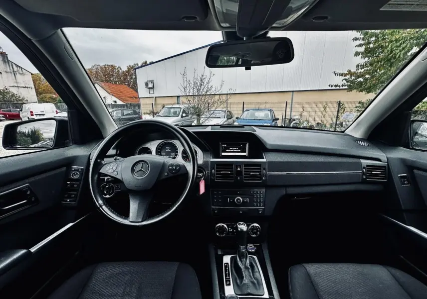 Vue intérieure avant du tableau de bord noir du Mercedes GLK 220 CDI 4-Matic avec volant multifonctions et écran central.