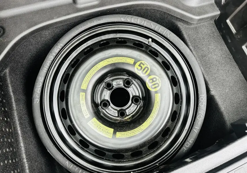 Gros plan sur la roue de secours compacte noire dans le coffre du Mercedes GLK 220 CDI 4-Matic noir de 2010.