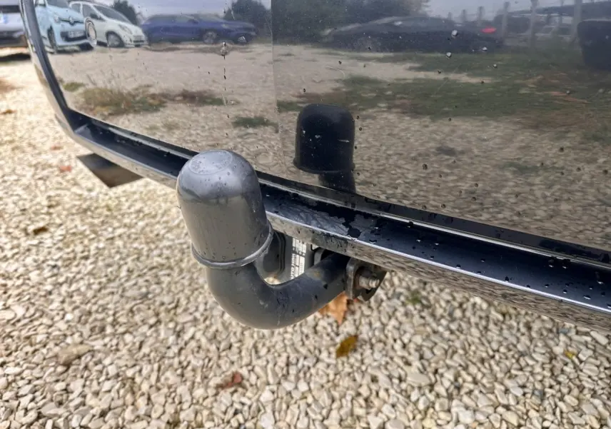 Gros plan sur l'attelage noir à l'arrière d'un Mercedes GLK 220 CDI noir, reflétant le sol gravillonné.