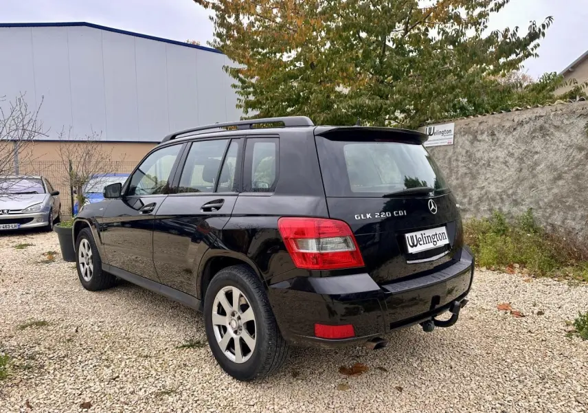 Vue 3/4 arrière droite d'un Mercedes GLK 220 CDI noir avec barres de toit et attelage visible.
