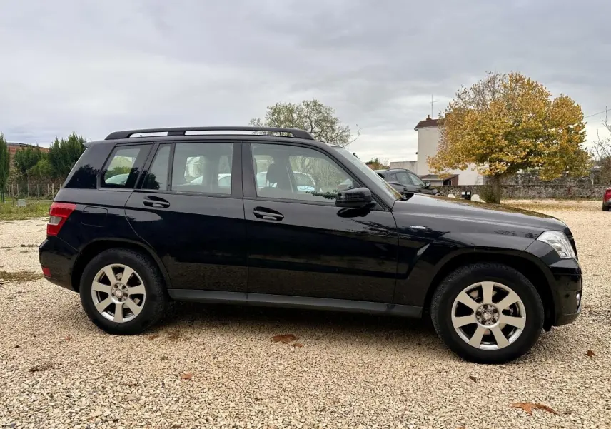 Profil côté gauche d'un Mercedes GLK noir 2010 garé sur un sol gravillonné avec toit ouvrant et jantes argentées.