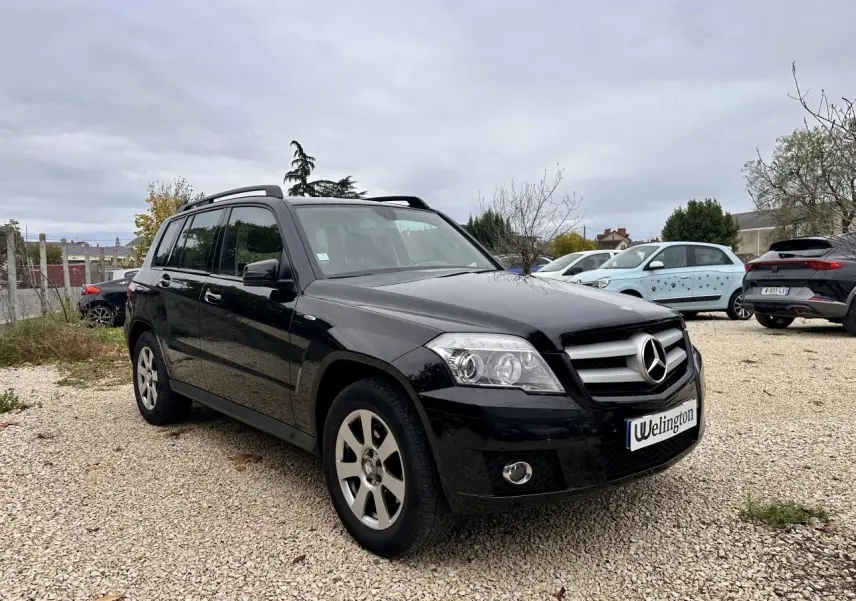 Mercedes GLK noir vue 3/4 avant droit sur parking avec calandre et jantes argentées visibles.