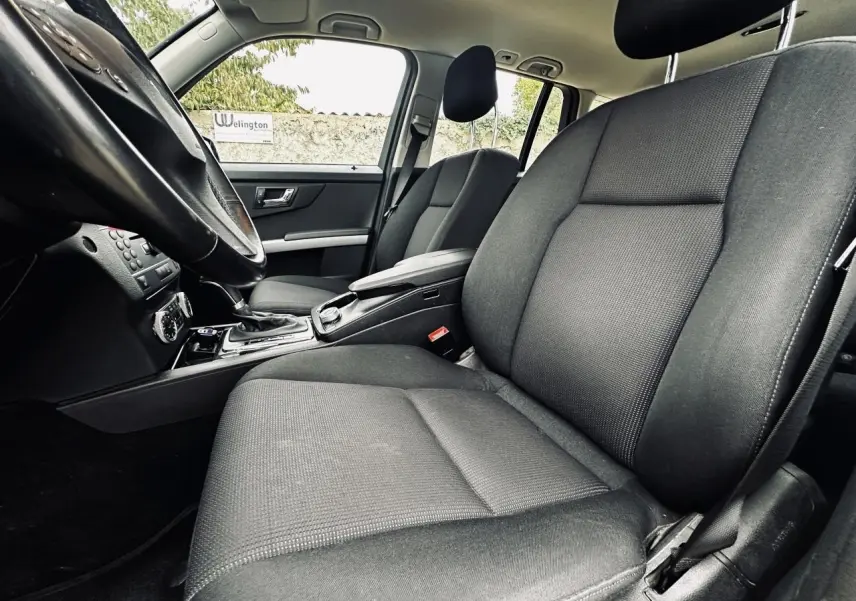 Vue intérieure côté conducteur du Mercedes GLK 220 CDI noir de 2010, mettant en valeur les sièges avant en tissu gris foncé.