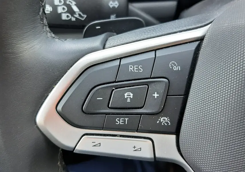 Gros plan sur les commandes de régulateur de vitesse au volant noir du Volkswagen T-Roc gris Indium 2024.